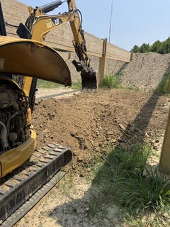 Excavator trenching alongside a retaining wall on a commercial site in Maryland